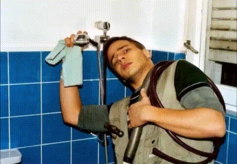 Szene aus dem misslungenen NDR-Radiofeature: Tom Wlaschiha als Klempner in einem blau gefliesten Badezimmer, mit Grimasse in der einen Hand einen Duschkopf mit Handtuch, in der anderen einen schwarzen Saugschlauch.